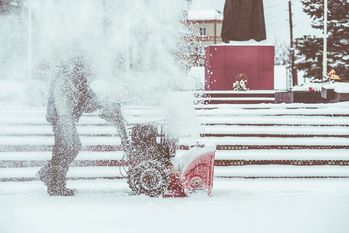 Mann räumt Betiebshof mit Schneefräse