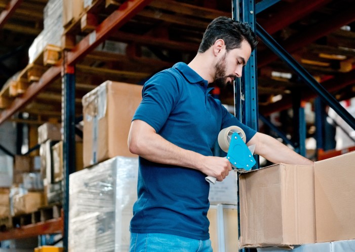 Mann im Lager, der einen Packbandabroller betätigt