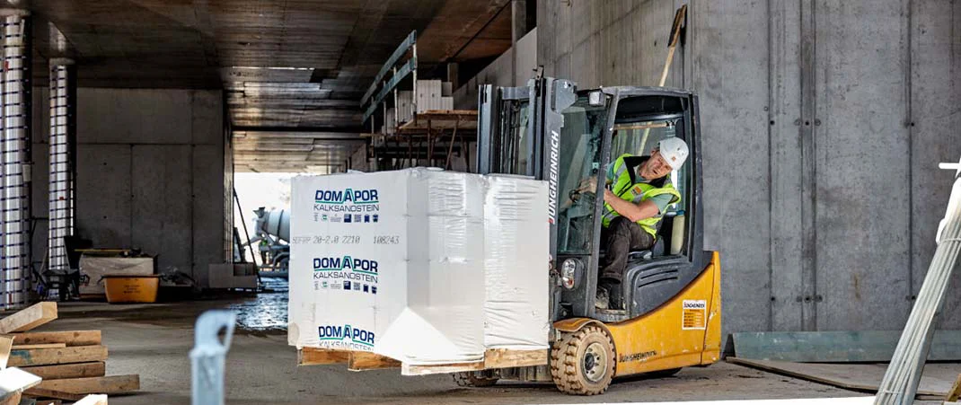 Mann fährt einen mit Baustoff beladenen Gabelstapler auf einer Baustelle
